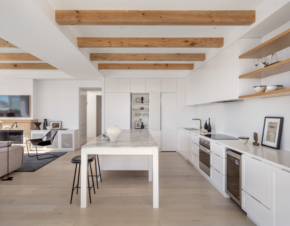 Idéer för funkis vitt kök med öppen planlösning, med vita skåp, marmorbänkskiva, vitt stänkskydd, ljust trägolv och en köksö