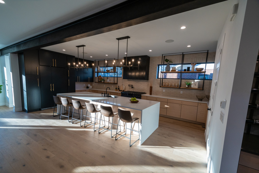 This is an example of a mid-sized modern galley open plan kitchen in Denver with an undermount sink, flat-panel cabinets, black cabinets, quartzite benchtops, white splashback, brick splashback, black appliances, medium hardwood floors, with island and white benchtop.