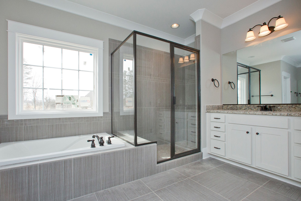 This is an example of a large transitional master bathroom in Raleigh with shaker cabinets, white cabinets, a drop-in tub, a corner shower, gray tile, grey walls, an undermount sink, grey floor and a hinged shower door.