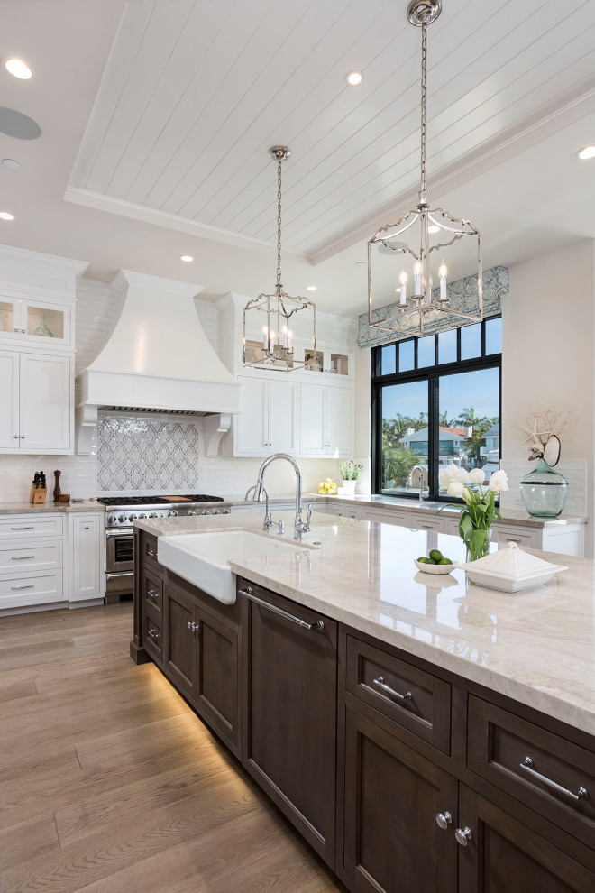 Photo of a traditional u-shaped kitchen in Orange County with a farmhouse sink, shaker cabinets, white cabinets, stainless steel appliances, medium hardwood floors, with island, brown floor, grey benchtop and recessed.