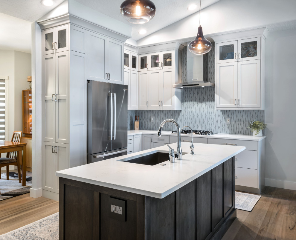 Foto på ett mellanstort funkis vit kök, med en undermonterad diskho, skåp i shakerstil, grå skåp, bänkskiva i kvarts, stänkskydd i porslinskakel, rostfria vitvaror, mellanmörkt trägolv, en köksö, brunt golv och blått stänkskydd