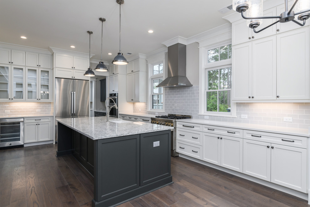 Transitional brown floor kitchen photo with a farmhouse sink, gray backsplash, subway tile backsplash, stainless steel appliances, an island and white countertops
