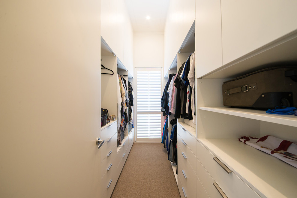 Expansive beach style gender-neutral walk-in wardrobe in Melbourne with flat-panel cabinets, white cabinets, carpet and beige floor.