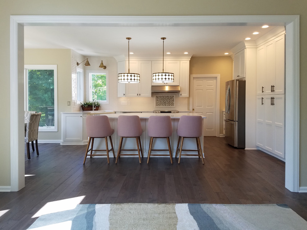 Large transitional u-shaped medium tone wood floor and gray floor eat-in kitchen photo with a farmhouse sink, shaker cabinets, white cabinets, quartz countertops, white backsplash, subway tile backsplash, stainless steel appliances, an island and white countertops