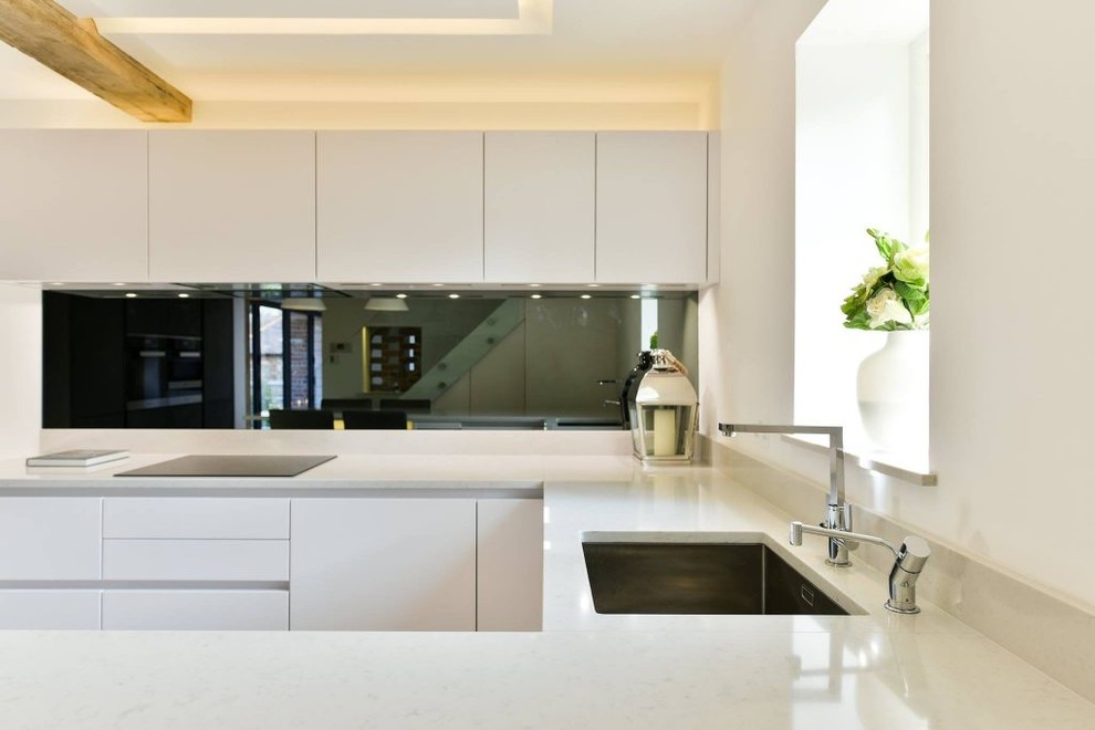 This is an example of a mid-sized contemporary u-shaped open plan kitchen in London with flat-panel cabinets, grey cabinets, quartz benchtops, stainless steel appliances, concrete floors, with island and beige floor.