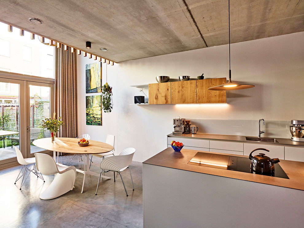 Mid-sized contemporary galley eat-in kitchen in Amsterdam with an integrated sink, flat-panel cabinets, grey cabinets, stainless steel benchtops, white splashback, glass sheet splashback, stainless steel appliances, concrete floors, with island and grey floor.