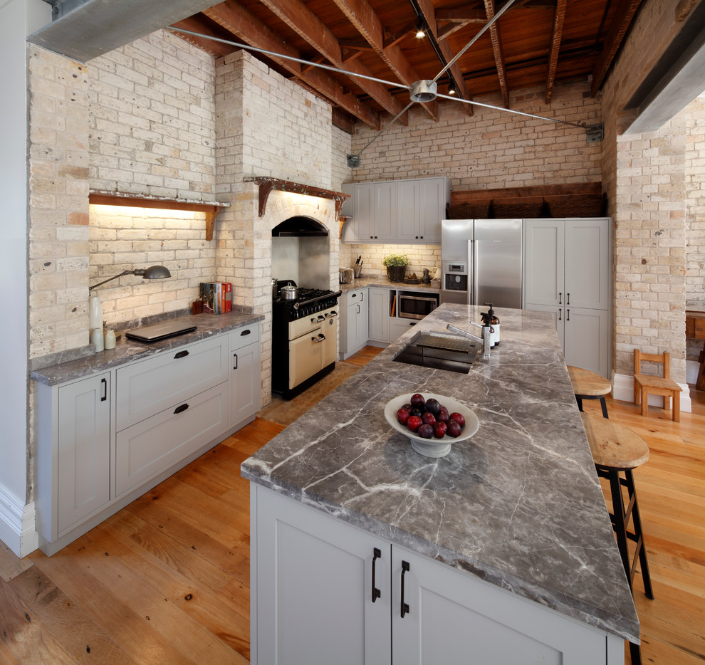 Photo of an industrial l-shaped eat-in kitchen in Sydney with an undermount sink, grey cabinets, marble benchtops, beige splashback, stainless steel appliances, black walls, medium hardwood floors and with island.