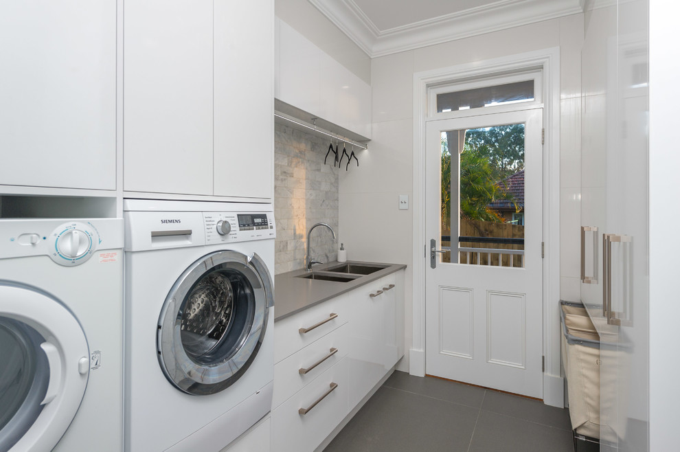 Inspiration for a transitional galley laundry room in Brisbane with an undermount sink, flat-panel cabinets, white cabinets, a side-by-side washer and dryer, quartz benchtops, white walls and porcelain floors.