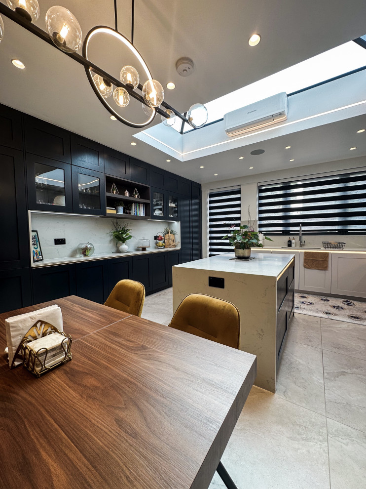 This is an example of a large traditional l-shaped kitchen/diner in London with a built-in sink, shaker cabinets, blue cabinets, quartz worktops, white splashback, engineered quartz splashback, integrated appliances, porcelain flooring, an island, beige floors, white worktops and feature lighting.