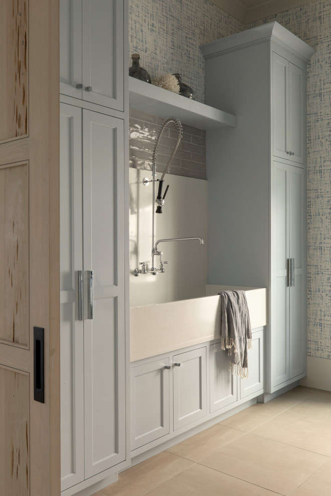 This is an example of a large beach style dedicated laundry room in Other with an utility sink, recessed-panel cabinets, grey cabinets, blue walls, ceramic floors, a stacked washer and dryer, beige floor, blue benchtop and wallpaper.