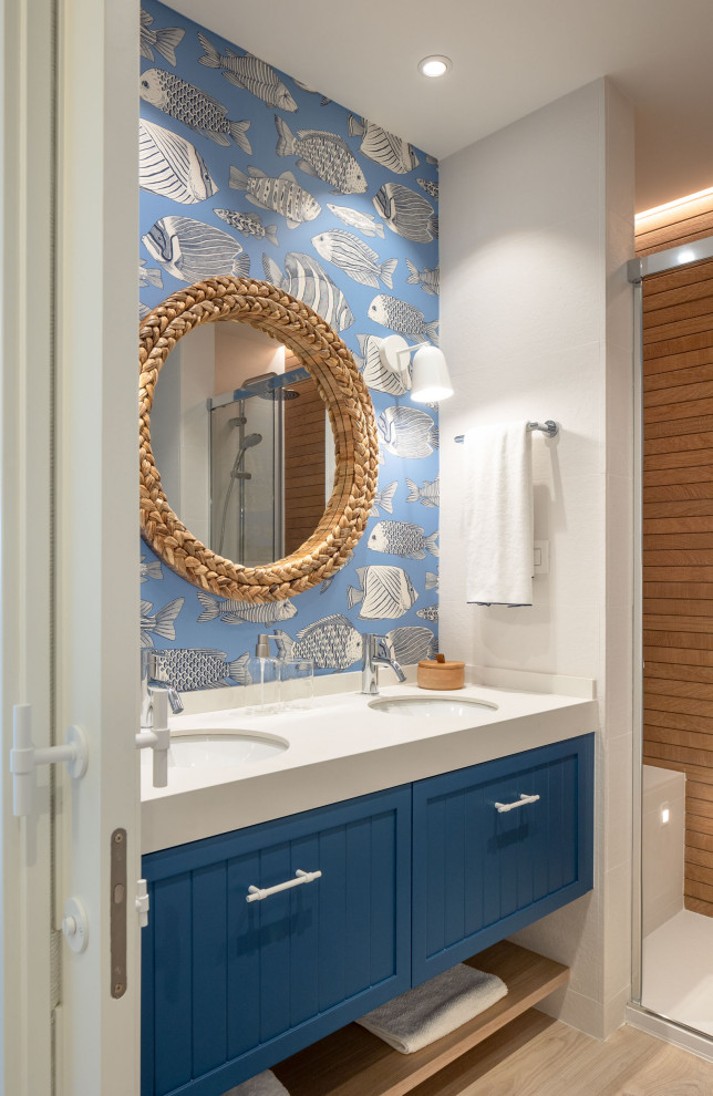 Пример оригинального дизайна: ванная комната среднего размера, в белых тонах с отделкой деревом в стиле неоклассика (современная классика) с фасадами с выступающей филенкой, белыми фасадами, душем без бортиков, инсталляцией, белой плиткой, керамической плиткой, синими стенами, полом из ламината, душевой кабиной, врезной раковиной, столешницей из искусственного кварца, коричневым полом, душем с раздвижными дверями, белой столешницей, тумбой под одну раковину и обоями на стенах