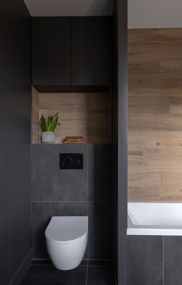 This is an example of a medium sized modern ensuite bathroom in Lyon with beaded cabinets, beige cabinets, a floating vanity unit, a submerged bath, a shower/bath combination, a wall mounted toilet, multi-coloured tiles, wood-effect tiles, black walls, slate flooring, solid surface worktops, black floors, white worktops, a single sink and wood walls.