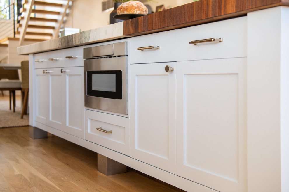 This is an example of a large nautical u-shaped kitchen/diner in New York with shaker cabinets, white cabinets, wood worktops, stainless steel appliances, medium hardwood flooring, an island, beige floors, multicoloured worktops and a vaulted ceiling.