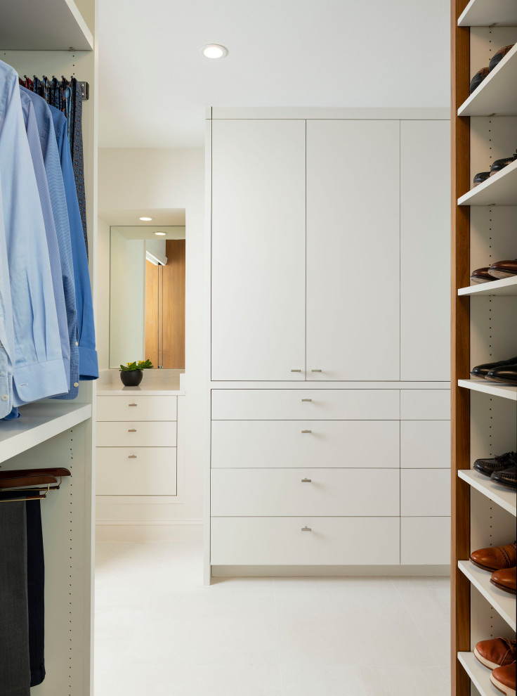 Modelo de armario y vestidor actual de tamaño medio con armarios con paneles lisos, puertas de armario de madera oscura, suelo de baldosas de porcelana y suelo blanco