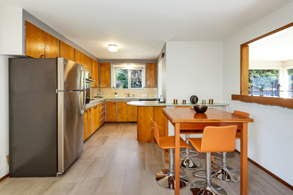 Photo of a midcentury eat-in kitchen in Seattle with laminate floors, flat-panel cabinets, medium wood cabinets, beige splashback, stainless steel appliances, a peninsula and beige floor.