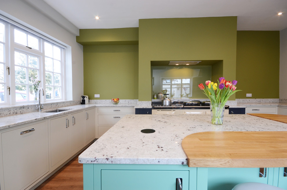 Photo of a medium sized contemporary u-shaped enclosed kitchen with a built-in sink, flat-panel cabinets, blue cabinets, granite worktops, glass sheet splashback, integrated appliances, laminate floors, an island and white worktops.