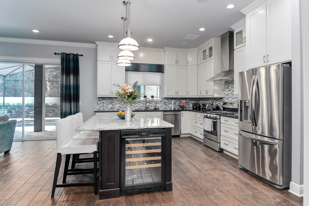 This is an example of a large transitional galley open plan kitchen in Orlando with recessed-panel cabinets, white cabinets, granite benchtops, grey splashback, glass tile splashback, stainless steel appliances, plywood floors and with island.