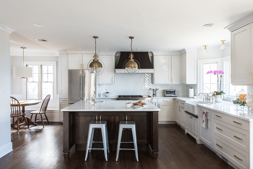 Inspiration for a mid-sized transitional l-shaped eat-in kitchen in New York with a farmhouse sink, flat-panel cabinets, white cabinets, quartz benchtops, white splashback, ceramic splashback, stainless steel appliances, medium hardwood floors, with island, brown floor and white benchtop.