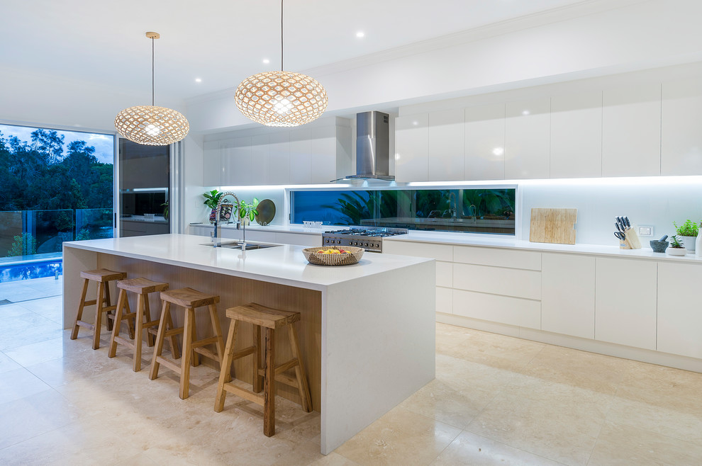 Photo of a large beach style galley open plan kitchen in Gold Coast - Tweed with an undermount sink, flat-panel cabinets, white cabinets, white splashback, window splashback, stainless steel appliances, with island and beige floor.
