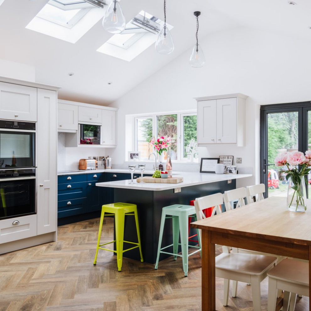 Inspiration for a mid-sized transitional u-shaped kitchen in Sussex with an undermount sink, shaker cabinets, medium hardwood floors, a peninsula, brown floor, vaulted, blue cabinets, quartzite benchtops, white splashback, stone slab splashback, panelled appliances and white benchtop.