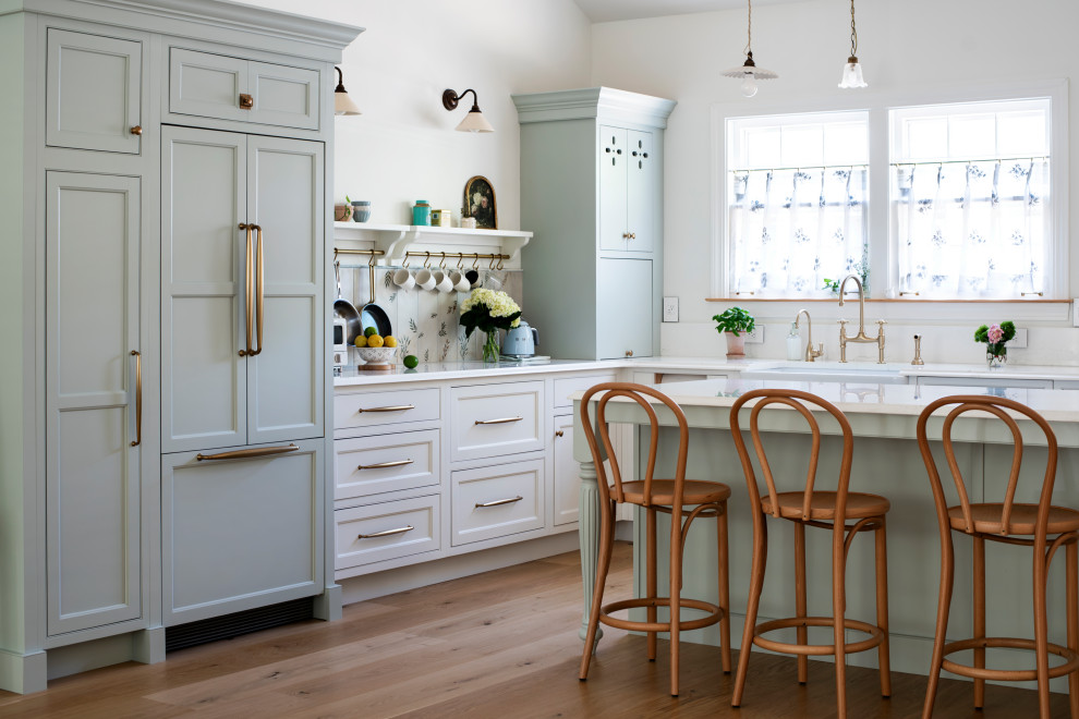Example of a large french country l-shaped medium tone wood floor, brown floor and vaulted ceiling open concept kitchen design in Nashville with a farmhouse sink, beaded inset cabinets, green cabinets, quartzite countertops, white backsplash, ceramic backsplash, paneled appliances, an island and white countertops