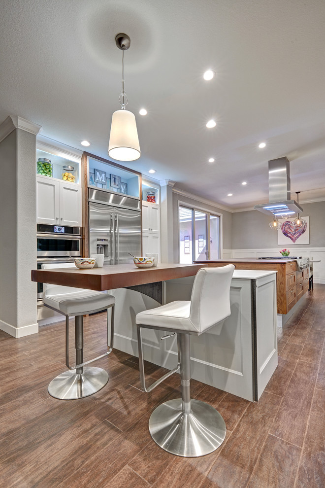 Inspiration for a large transitional galley eat-in kitchen in Sacramento with a farmhouse sink, recessed-panel cabinets, white cabinets, quartz benchtops, white splashback, porcelain splashback, stainless steel appliances, medium hardwood floors and multiple islands.