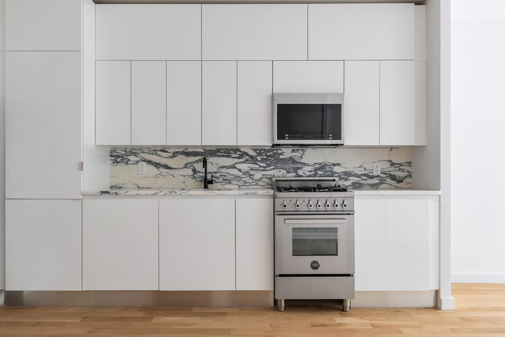 Inspiration för små moderna linjära flerfärgat kök med öppen planlösning, med en nedsänkt diskho, vita skåp, marmorbänkskiva, flerfärgad stänkskydd, stänkskydd i marmor, rostfria vitvaror och ljust trägolv