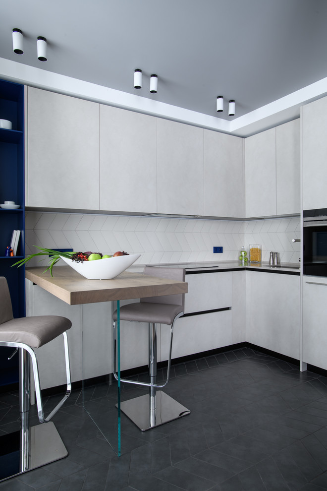 Contemporary l-shaped separate kitchen in Moscow with grey cabinets, white splashback, black appliances, black floor and black benchtop.