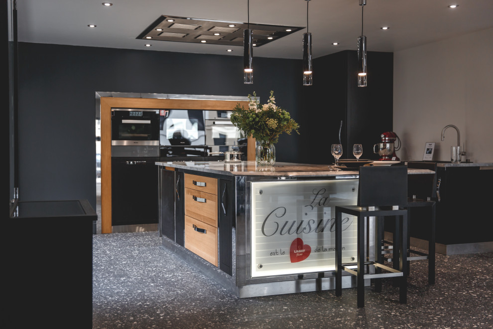 Large contemporary grey and black l-shaped open plan kitchen in Other with an integrated sink, all styles of cabinet, dark wood cabinets, granite worktops, black appliances, terrazzo flooring, an island, black floors, white worktops and a drop ceiling.
