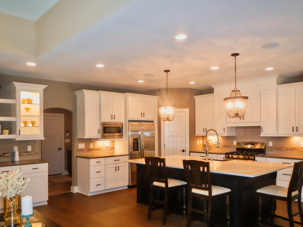 Inspiration for a mid-sized transitional l-shaped medium tone wood floor and brown floor open concept kitchen remodel with a farmhouse sink, shaker cabinets, dark wood cabinets, quartz countertops, gray backsplash, ceramic backsplash, stainless steel appliances, an island and multicolored countertops