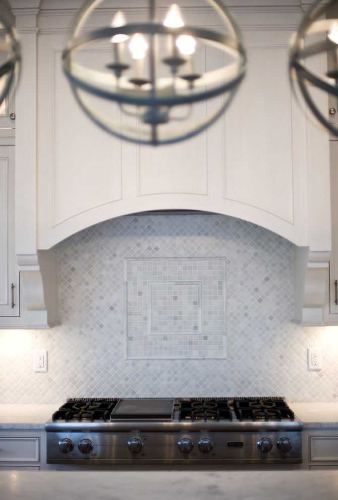 Example of a transitional kitchen design with an undermount sink, recessed-panel cabinets, white cabinets, marble countertops, white backsplash, mosaic tile backsplash, stainless steel appliances and an island