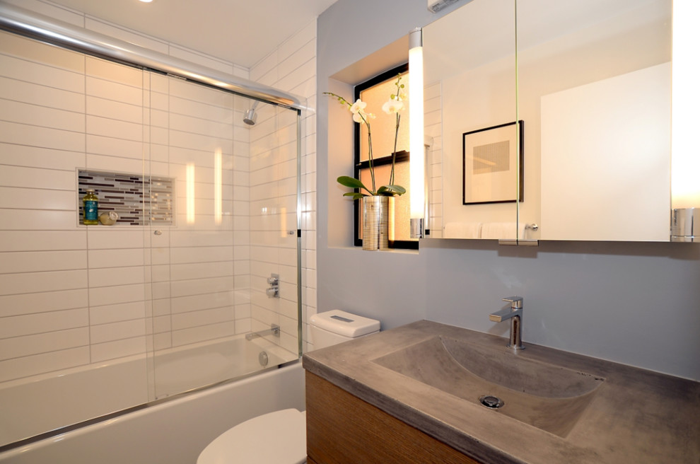Inspiration for a small contemporary 3/4 bathroom in San Francisco with flat-panel cabinets, medium wood cabinets, an alcove tub, a shower/bathtub combo, a two-piece toilet, white tile, grey walls, an integrated sink, concrete benchtops, a sliding shower screen and grey benchtops.