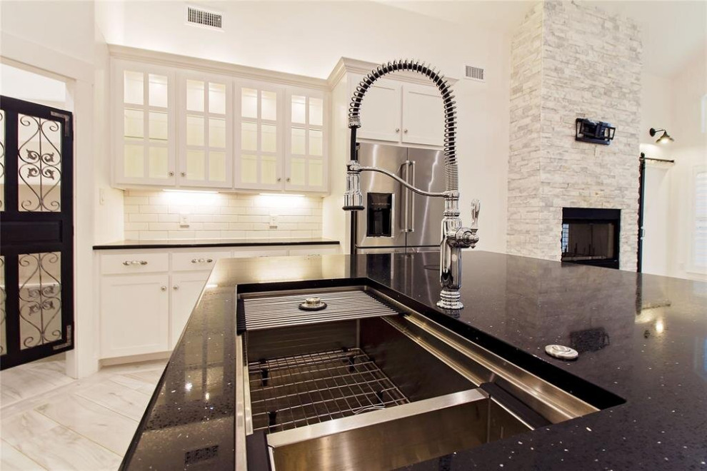 Photo of a mid-sized transitional l-shaped eat-in kitchen in Houston with a triple-bowl sink, shaker cabinets, white cabinets, quartzite benchtops, white splashback, ceramic splashback, stainless steel appliances, porcelain floors, with island, multi-coloured floor, black benchtop and coffered.