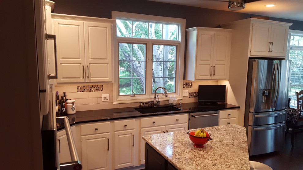 Inspiration for a mid-sized transitional l-shaped medium tone wood floor and brown floor kitchen remodel with an undermount sink, raised-panel cabinets, white cabinets, granite countertops, white backsplash, subway tile backsplash, stainless steel appliances and an island