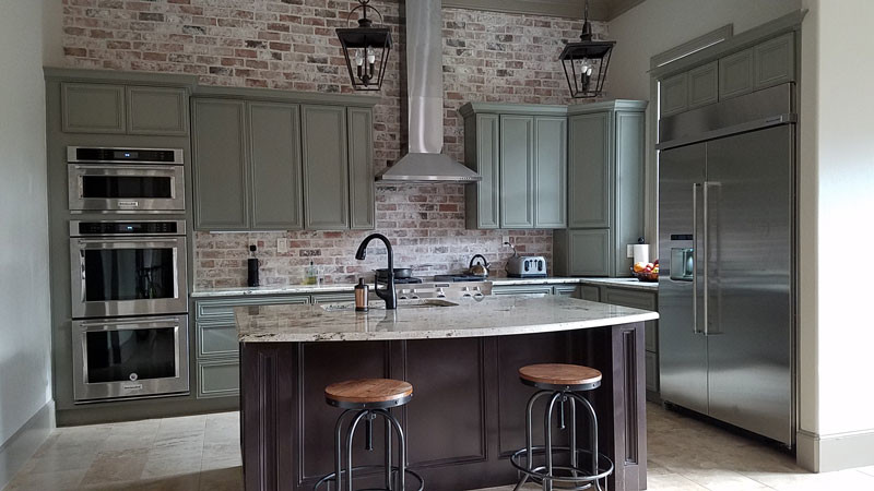 Inspiration for a mid-sized industrial l-shaped eat-in kitchen in Houston with an undermount sink, recessed-panel cabinets, green cabinets, granite benchtops, red splashback, brick splashback, stainless steel appliances, ceramic floors, with island and beige floor.
