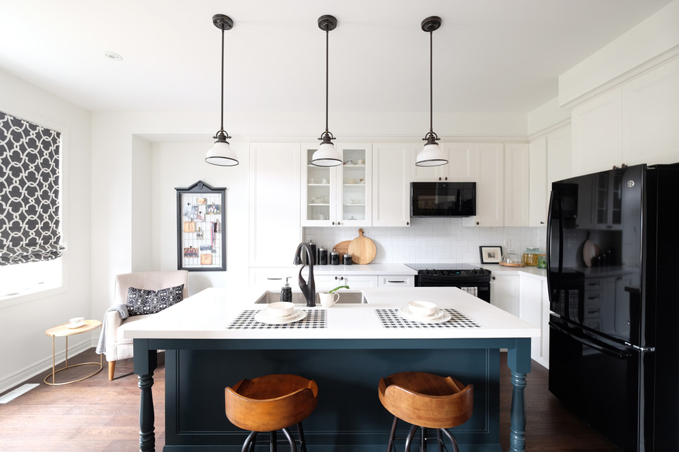 Inspiration for a transitional l-shaped dark wood floor and brown floor kitchen remodel in Toronto with an undermount sink, white cabinets, white backsplash, black appliances, an island, white countertops and recessed-panel cabinets