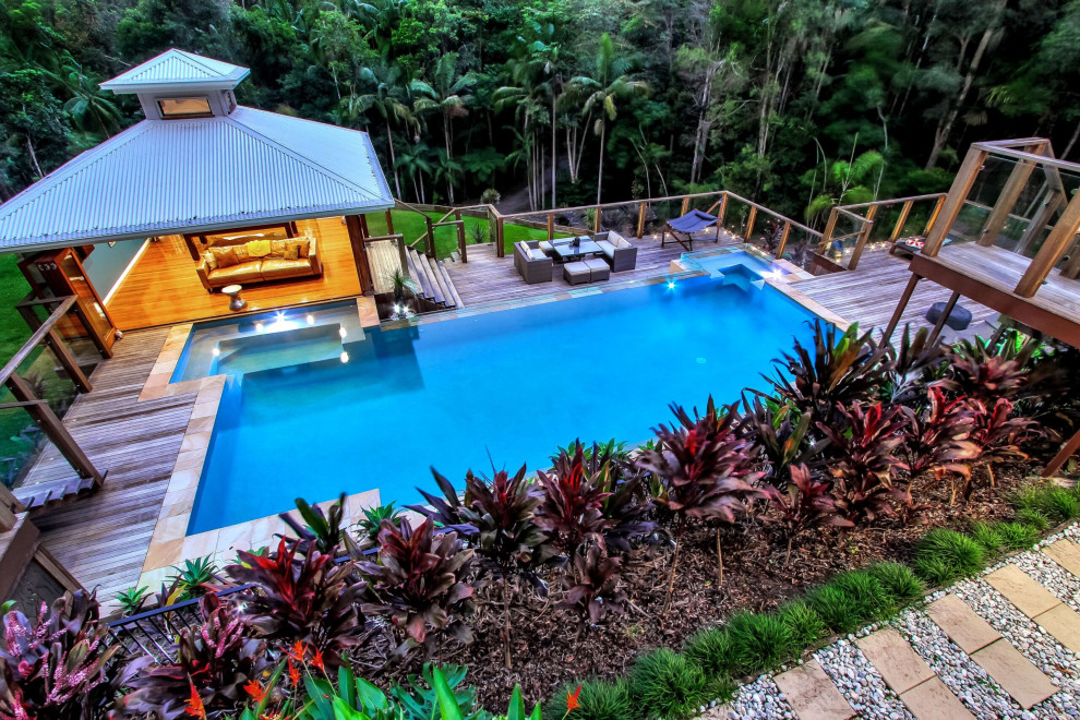 Inspiration for a large tropical backyard custom-shaped aboveground pool in Other with a pool house and decking.