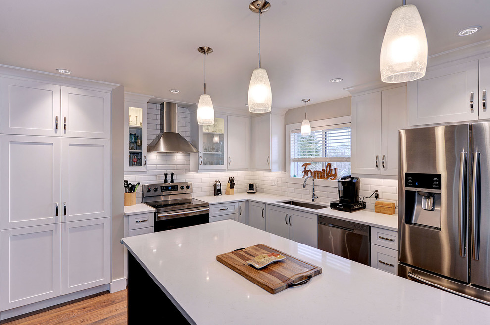 Example of a transitional dark wood floor and brown floor enclosed kitchen design with a single-bowl sink, shaker cabinets, white cabinets, quartzite countertops, white backsplash, subway tile backsplash, stainless steel appliances and an island