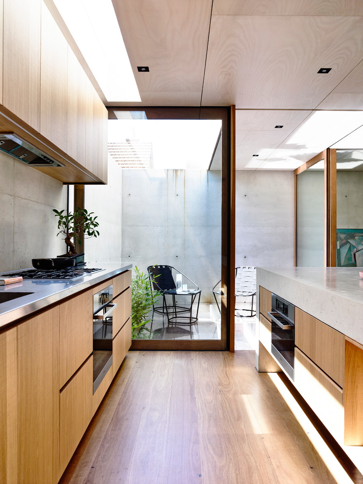 Inspiration for a small modern galley kitchen in Melbourne with a double-bowl sink, medium wood cabinets, concrete benchtops, grey splashback, medium hardwood floors, with island and stainless steel appliances.