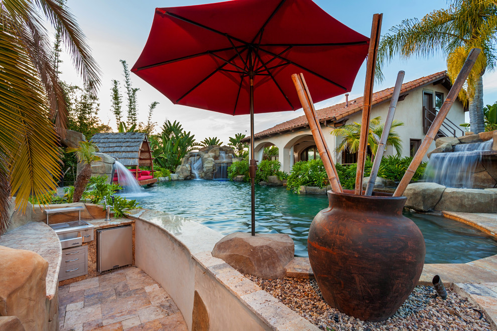 Expansive tropical backyard custom-shaped natural pool in San Diego with natural stone pavers and a water slide.