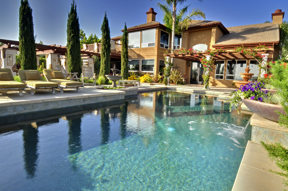 Photo of a large mediterranean backyard custom-shaped infinity pool in Orange County with concrete slab.