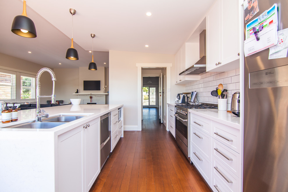 Inspiration for a small scandinavian single-wall eat-in kitchen in Hobart with a double-bowl sink, recessed-panel cabinets, white cabinets, granite benchtops, white splashback, ceramic splashback, stainless steel appliances, medium hardwood floors and with island.