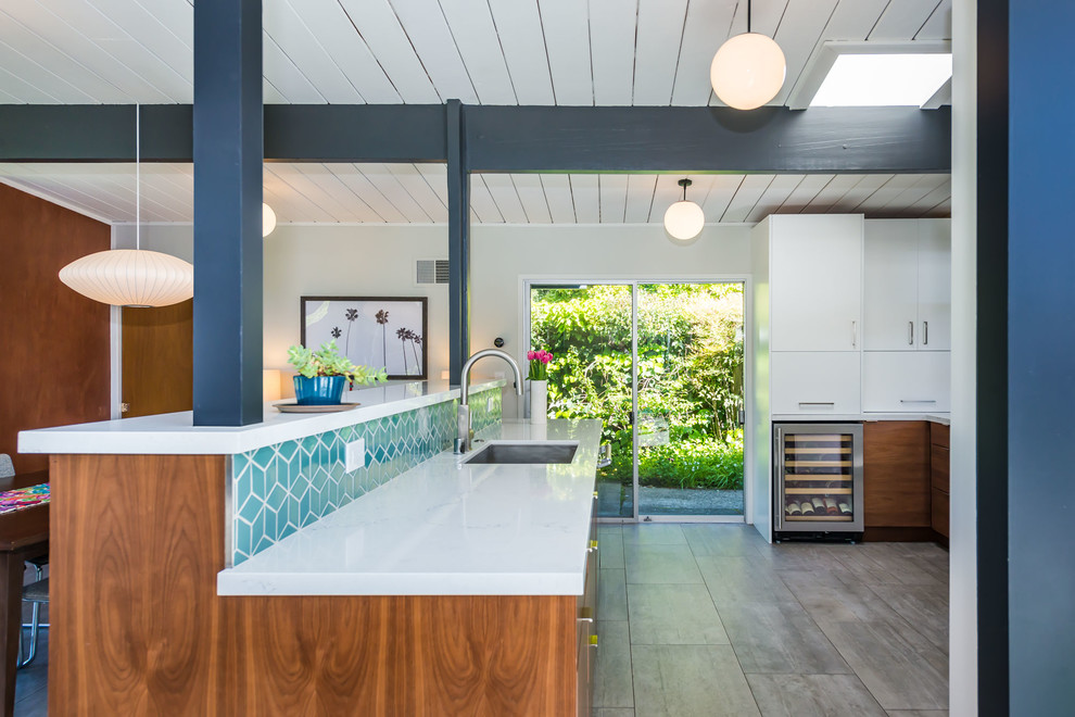 Inspiration for a mid-sized midcentury single-wall open plan kitchen in San Francisco with a drop-in sink, flat-panel cabinets, white cabinets, quartzite benchtops, blue splashback, ceramic splashback, stainless steel appliances, painted wood floors, a peninsula, grey floor and white benchtop.