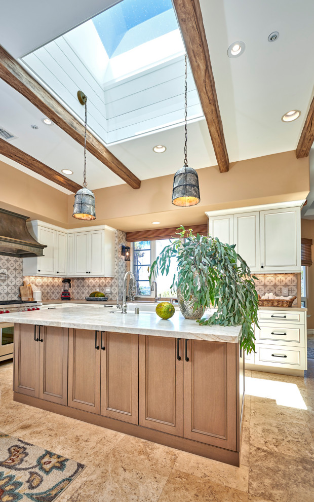 Example of a mid-sized mountain style galley travertine floor, beige floor and exposed beam open concept kitchen design in Denver with a farmhouse sink, recessed-panel cabinets, white cabinets, quartz countertops, multicolored backsplash, stone tile backsplash, stainless steel appliances, an island and brown countertops