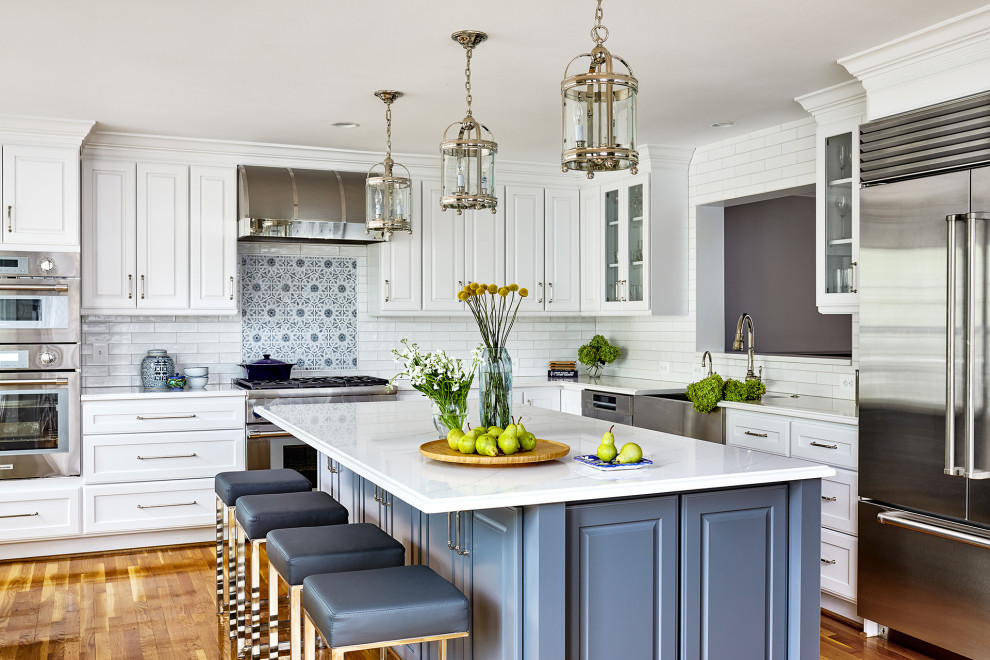 Design ideas for a medium sized classic l-shaped kitchen in DC Metro with a belfast sink, raised-panel cabinets, white cabinets, engineered stone countertops, white splashback, metro tiled splashback, stainless steel appliances, medium hardwood flooring, brown floors and white worktops.