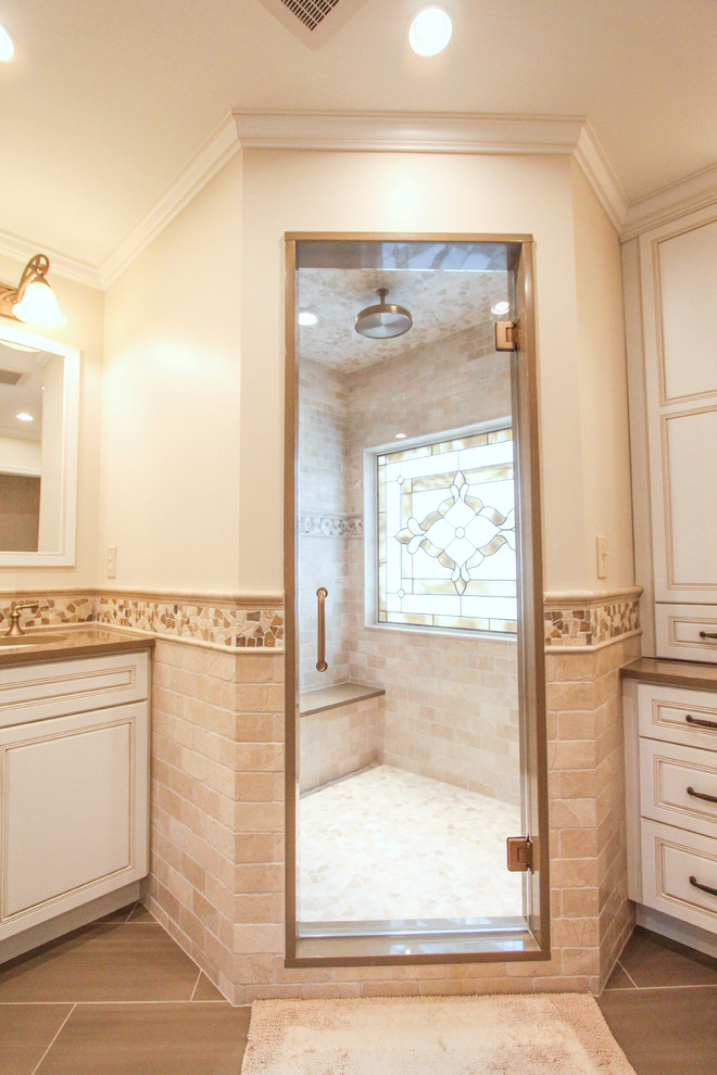 Photo of a mid-sized traditional master bathroom in Cincinnati with an undermount sink, flat-panel cabinets, white cabinets, engineered quartz benchtops, a corner shower, beige tile, stone tile, beige walls and porcelain floors.