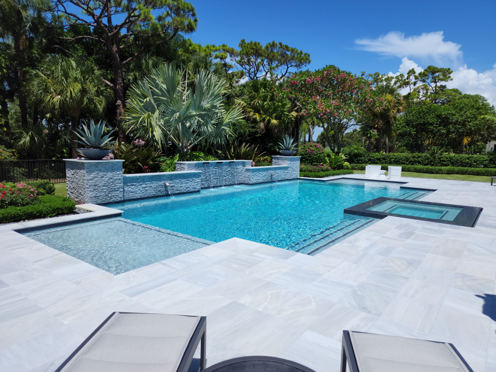 Photo of a large modern backyard pool in Miami with natural stone pavers.