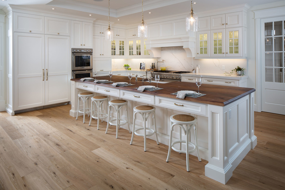 Inspiration for a large traditional l-shaped eat-in kitchen in Toronto with a farmhouse sink, white cabinets, wood benchtops, stone slab splashback, stainless steel appliances, with island, beige floor, brown benchtop, recessed-panel cabinets, white splashback and light hardwood floors.