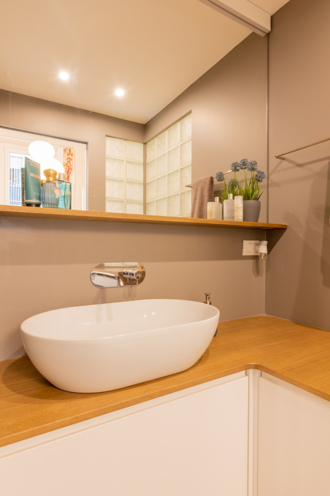 Exempel på ett litet modernt beige beige badrum med dusch, med släta luckor, vita skåp, en toalettstol med separat cisternkåpa, grå kakel, grå väggar, ljust trägolv, ett fristående handfat, träbänkskiva, beiget golv och dusch med gångjärnsdörr