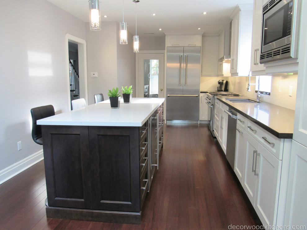 Example of a large transitional l-shaped dark wood floor enclosed kitchen design in Toronto with an undermount sink, shaker cabinets, white cabinets, quartz countertops, white backsplash, stone slab backsplash, stainless steel appliances and an island